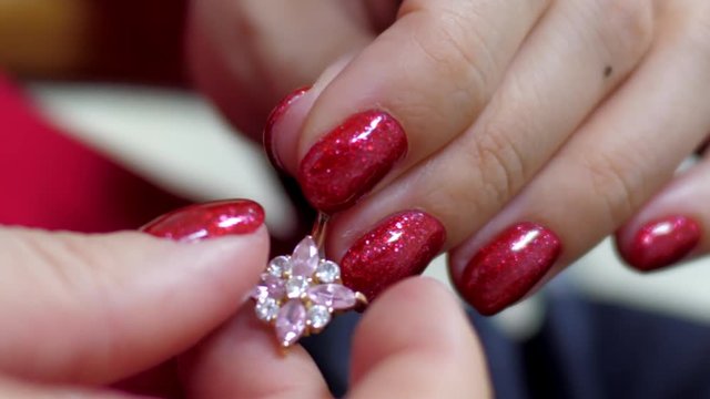 slow motion close view girl with modern bright red manicure examines gold navel piercing banana with turning ball