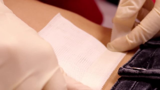 closeup slow motion skilled master fixes large white cotton napkin on girl belly with patch after piercing 