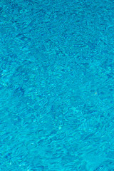 Blue water in swimming pool background. Ripple Water in swimming pool with sun reflection. Blue swimming pool rippled water detail. vertical photo.
