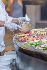 A cook in a restaurant fries food on a large iron firebox. vertical photo.