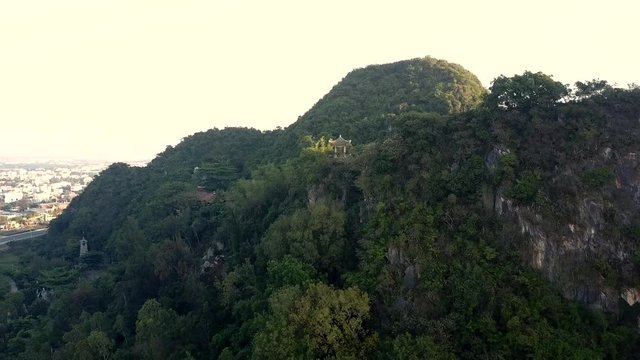 aerial wonderful picture dark forestry hill with temple buildings near city against bright clear sky in summer morning
