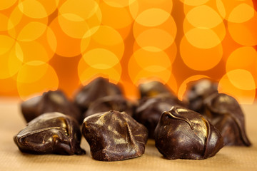 Close up of fresh, delicious and healthy homemade raw chocolate bonbons with golden sprinkles against orange blurred background with lights bokeh
