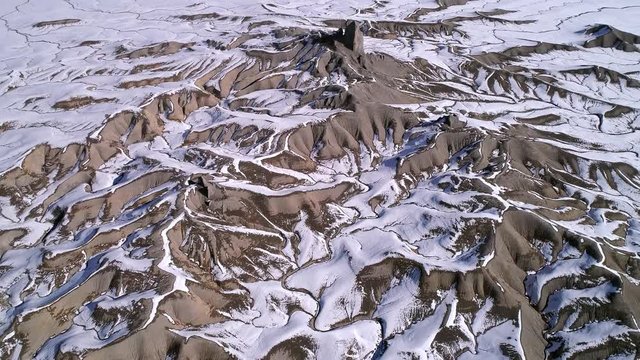 Aerial view flying over desert terrain as snow melts eroding the the Utah landscape.