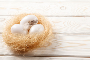 Easter background. Easter white eggs and feather in nest on rustic white wooden background. Close-up, copy space