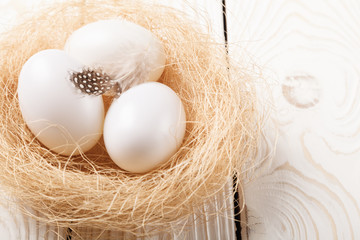 Easter background. Easter white eggs and feather in nest on rustic white wooden background. Close-up, copy space