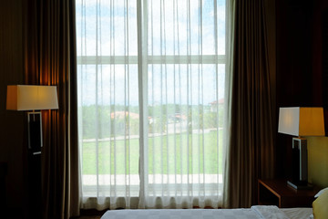 Fototapeta na wymiar White curtain at window in a bedroom to green garden outside