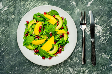 salad with avocado, arugula, spinach, pomegranate, seeds on a concrete background