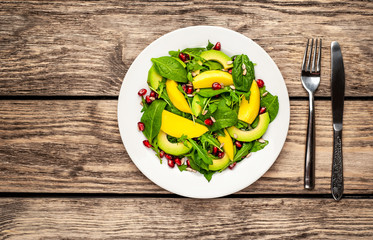 salad with avocado, arugula, spinach, pomegranate, seeds on wooden background