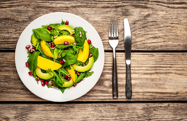 salad with avocado, arugula, spinach, pomegranate, seeds on wooden background