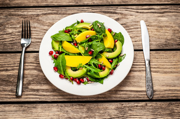 salad with avocado, arugula, spinach, pomegranate, seeds on wooden background