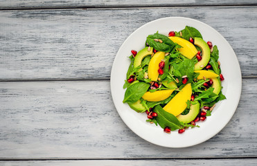 salad with avocado, arugula, spinach, pomegranate, seeds on wooden background