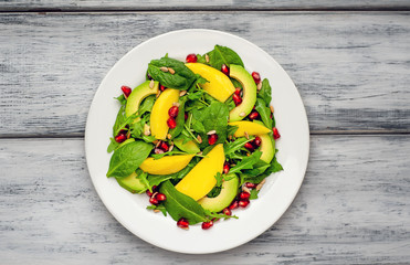salad with avocado, arugula, spinach, pomegranate, seeds on wooden background