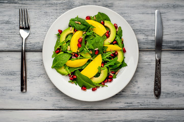 salad with avocado, arugula, spinach, pomegranate, seeds on wooden background