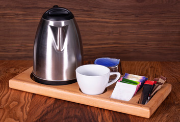 Group of coffee making set in a hotel room with stainless steel electric kettle, clean cup, teaspoon. Front view with copy space.