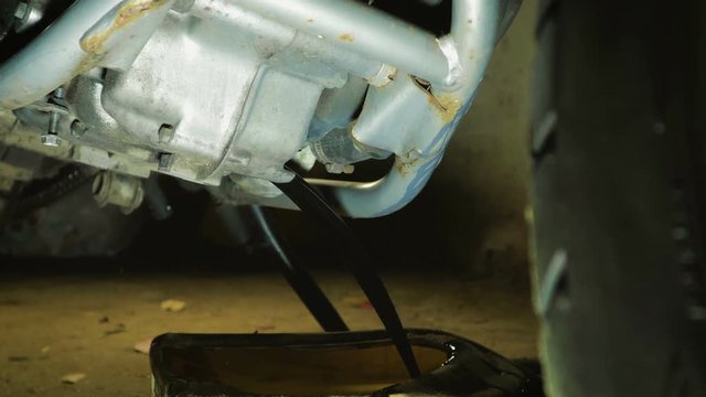 Close-up of the motorcycle engine crankcase with merging old waste oil into a plastic canister