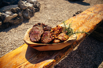 Delicious grilled pork and chicken meat with rosemary on the traditional wooden dish near the barbecue fireplace