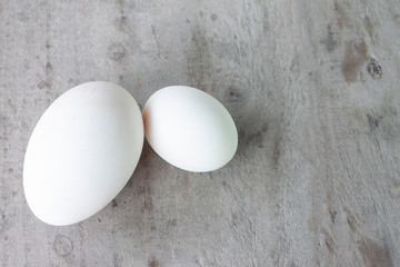 Compare size goose egg and duck egg on old wooden table background.