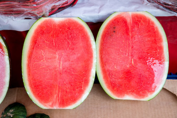 Sweet water melon, some cut half. watermelon at market. Fresh organic watermelons on a marketplace. Slices of watermelon in transparent plastic foil . Pile of watermelons. Melon background.