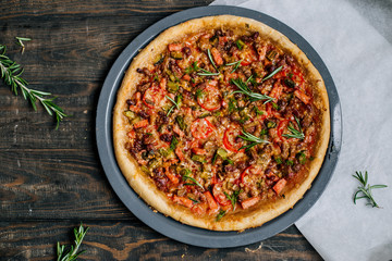 Pizza with tomatoes, meat, cucumbers and sausages on a wooden table top view