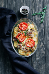 Baked pork with potatoes and tomatoes and rosemary on wooden table top view