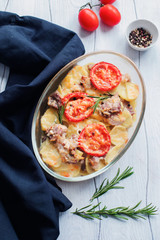 Baked pork with potatoes and tomatoes and rosemary on wooden table top view