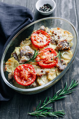 Baked pork with potatoes and tomatoes and rosemary on wooden table top view