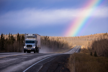 Cube semit truck on wet asphalt road with colorful rainbow over late fall forest landscape after...
