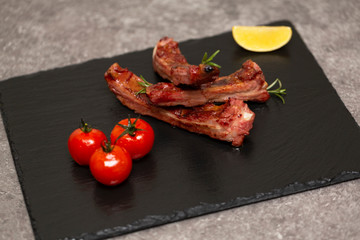 Pork ribs in barbecue sauce and honey roasted tomatoes on a black slate dish. Top view with copy space