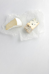 Camembert and blue cheese on parchment paper. Pieces of various cheese on white background. Dorblu and soft cheese in the style of minimalism. Eco-friendly dairy products