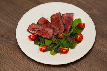 Juicy steak medium rare beef with green salad and tomatoes on white plate