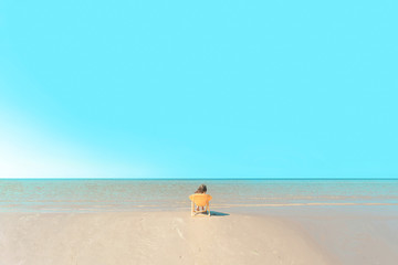 Fototapeta na wymiar little girl by the sea.little girl resting on the beach.little girl sitting on a yellow chair on the beach and looks into the distance . the sea is calm, the sky is cloudless.hair fluttering in the wi