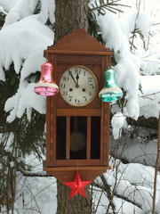 Clock decorated with Christmas toys in the winter forest on a fir covered with snow.