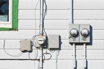 Electric power supply meters and phone line drop junction box on exterior white vinyl siding wall...