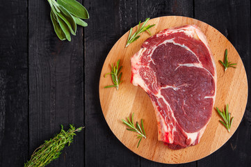 Raw beef steak on cutting board with herbs for cooking meat. Sage thyme and rosemary. Top view.