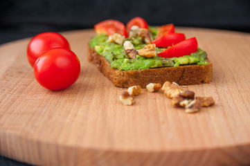 Toast with avocado walnut and cherry tomatoes on wooden cutting board.