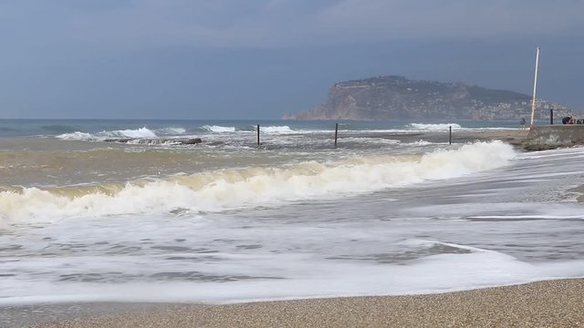 Alanya beach waves with fisherman and Bedesten Alanya fortress island on background