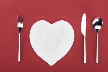 view from above of heart shaped plate and cutlery isolated on red, st valentine day concept