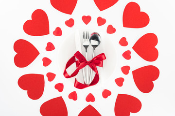 elevated view of cutlery wrapped by red festive ribbon surrounded by heart symbols isolated on white, st valentine day concept