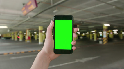 Lublin, Poland - July 2018: A hand holding a phone with a green screen in an underground parking lot. Close-up shot. Soft focus