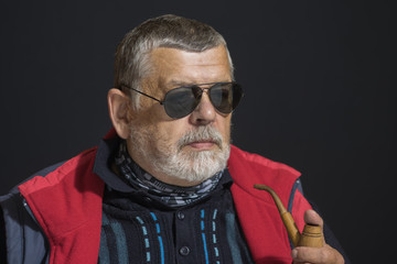 Nice low key portrait of senior man in black eyeglasses holding tobacco-pipe
