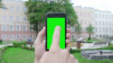 Lublin, Poland - July 2018: A hand holding a phone with a green screen in a public park. Close-up shot. Soft focus