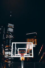 basketball rim with ball in it, in front of skyscrapers, night lights