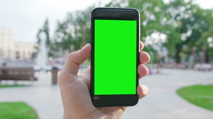 Lublin, Poland - July 2018: A hand holding a phone with a green screen in a public park. Close-up shot. Soft focus