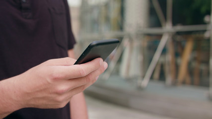A close-up of a man's hand holding and using a phone outdoors. Soft focus
