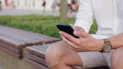 An attractive young man sitting and using a phone in town. Close-up shot. Soft focus