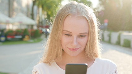 Fototapeta premium An attractive young blonde lady using a phone in town. Close-up shot. Soft focus