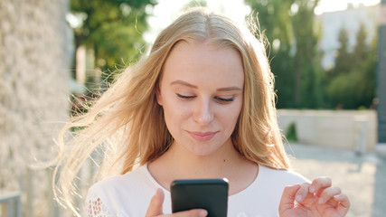 An attractive young blonde lady using a phone in town. Close-up shot. Soft focus