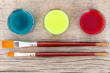 Water colors of aquamarine, yellow and red colours with brushes on a wooden surface. View from above. Close-up.