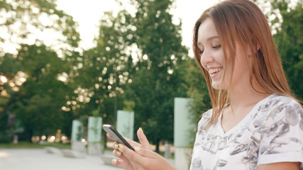 Fototapeta premium An attractive young lady using a phone in town while walking. Medium dolly shot. Soft focus