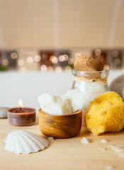Replacing cosmetic products with natural coconut oil moisturizer cream. Solid coconut oil chuncs in wooden cup in with oder body care products in brown beige tile bathroom. Cozy set bokeh.